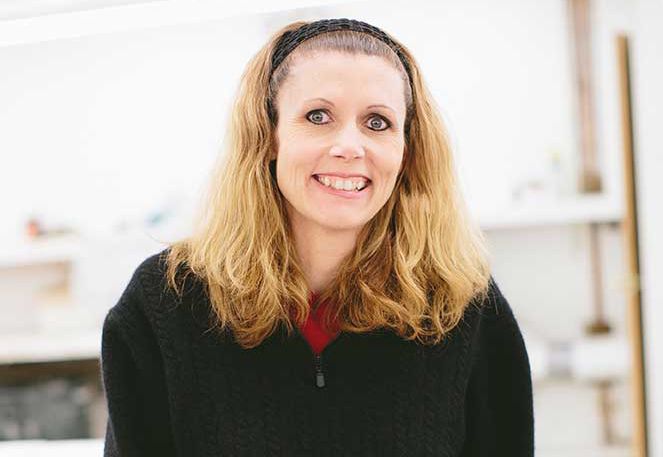 Woman with blonde hair smiling while wearing a black jacket and red shirt